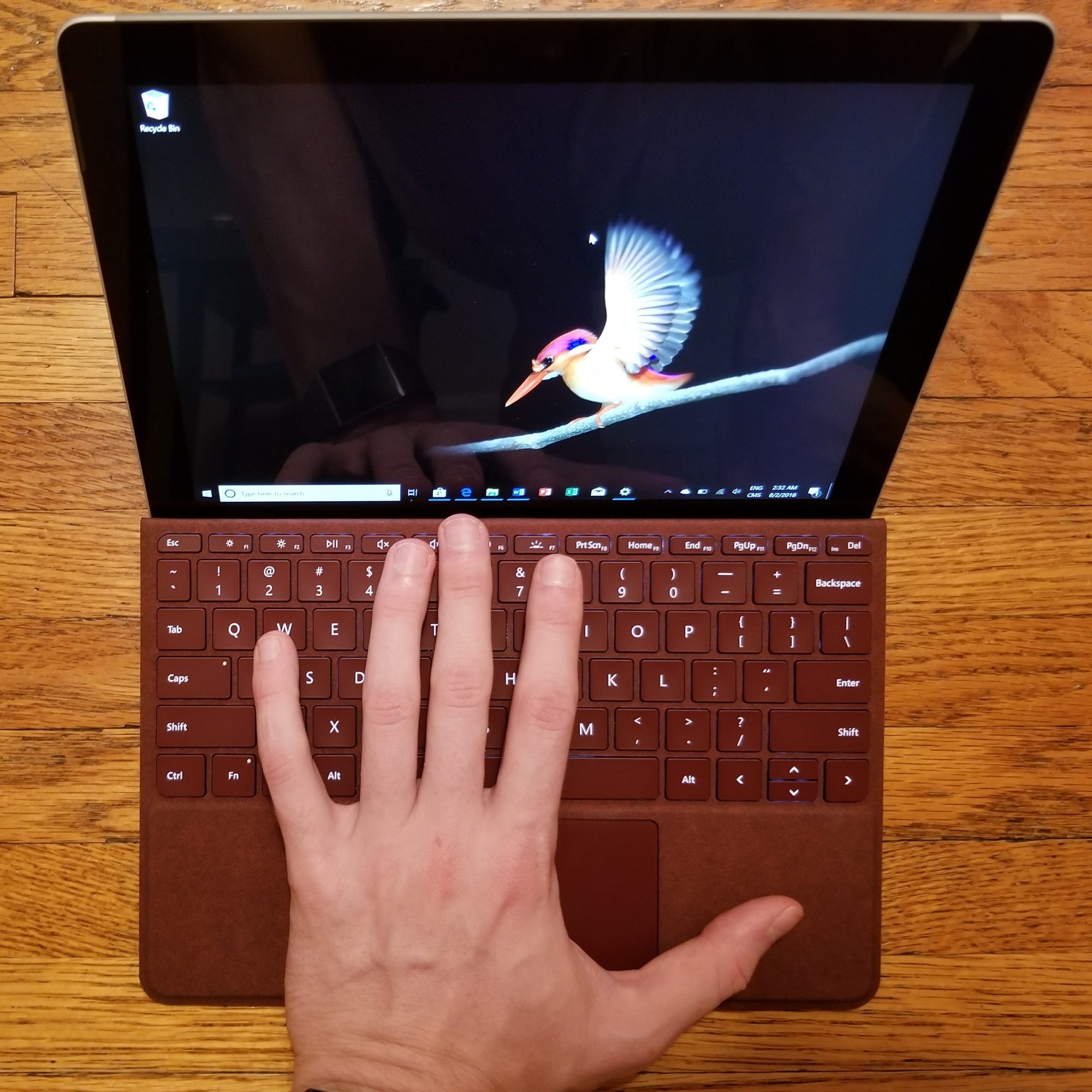 Surface Go with a left hand on the red Alcantara keyboard