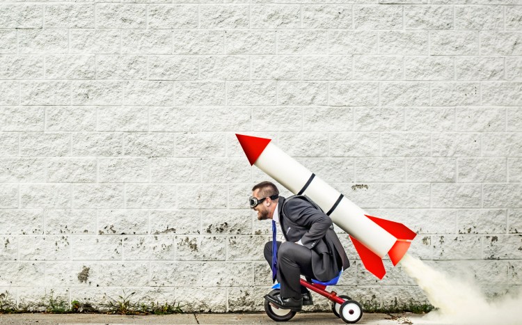 Businessman riding a tricycle and getting help from the rocket strapped to his back :-)