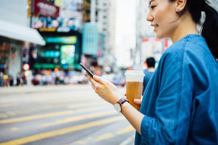 On a city street, a woman looks at her smartphone