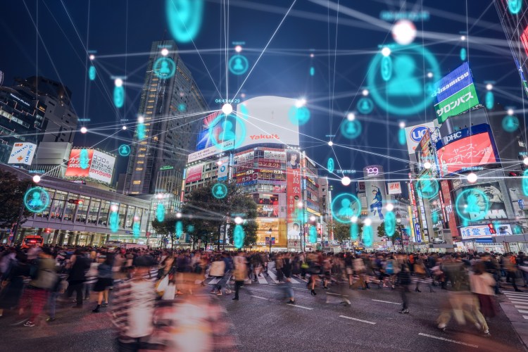 A busy street scene at night with digital personalization symbols above passersby